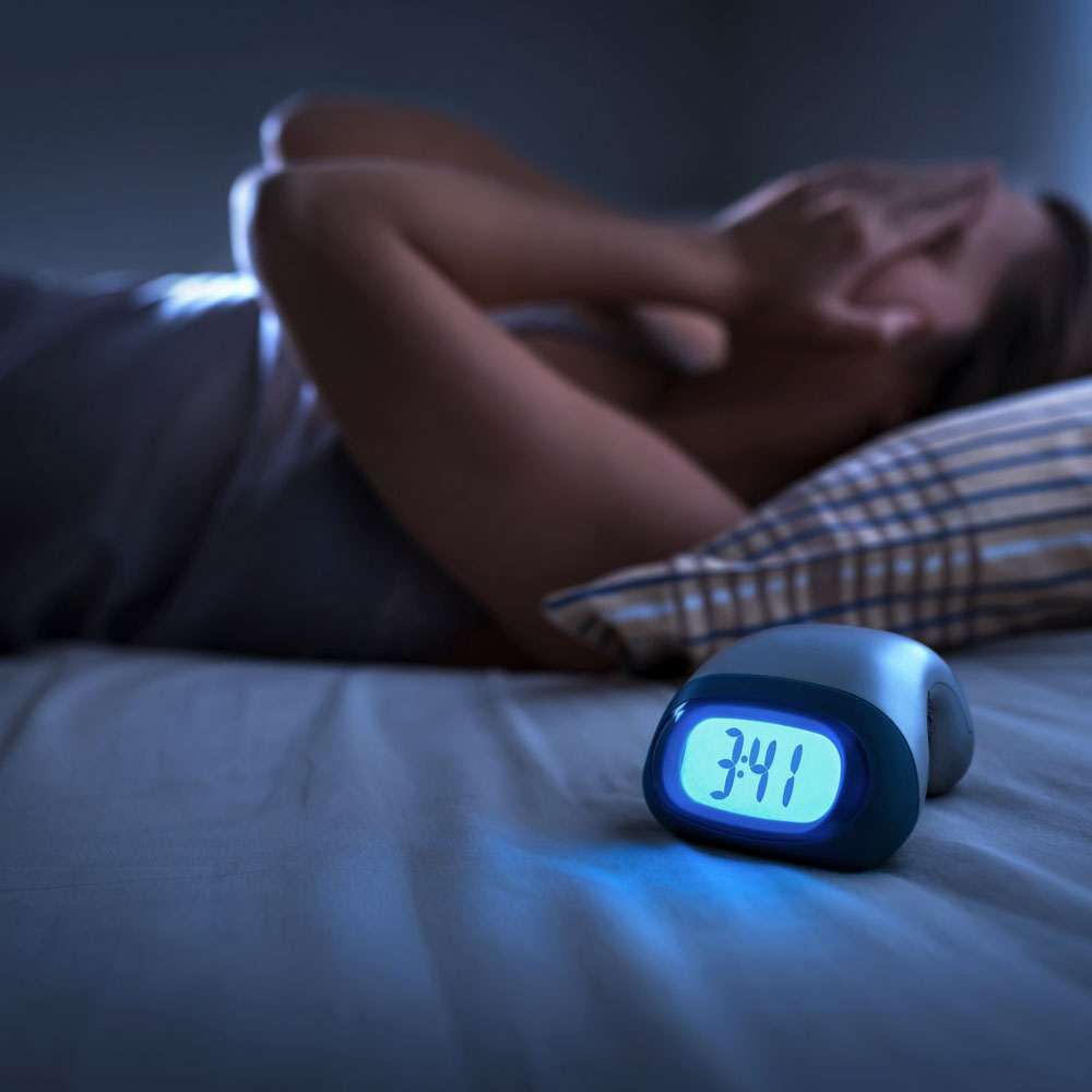 Overwhelmed nurse laying awake in bed at 3:41 AM, suffering from insomnia caused by unresolved trauma or PTSD, highlighting the need for professional insomnia treatment at Deer Hollow for first responders and veterans.