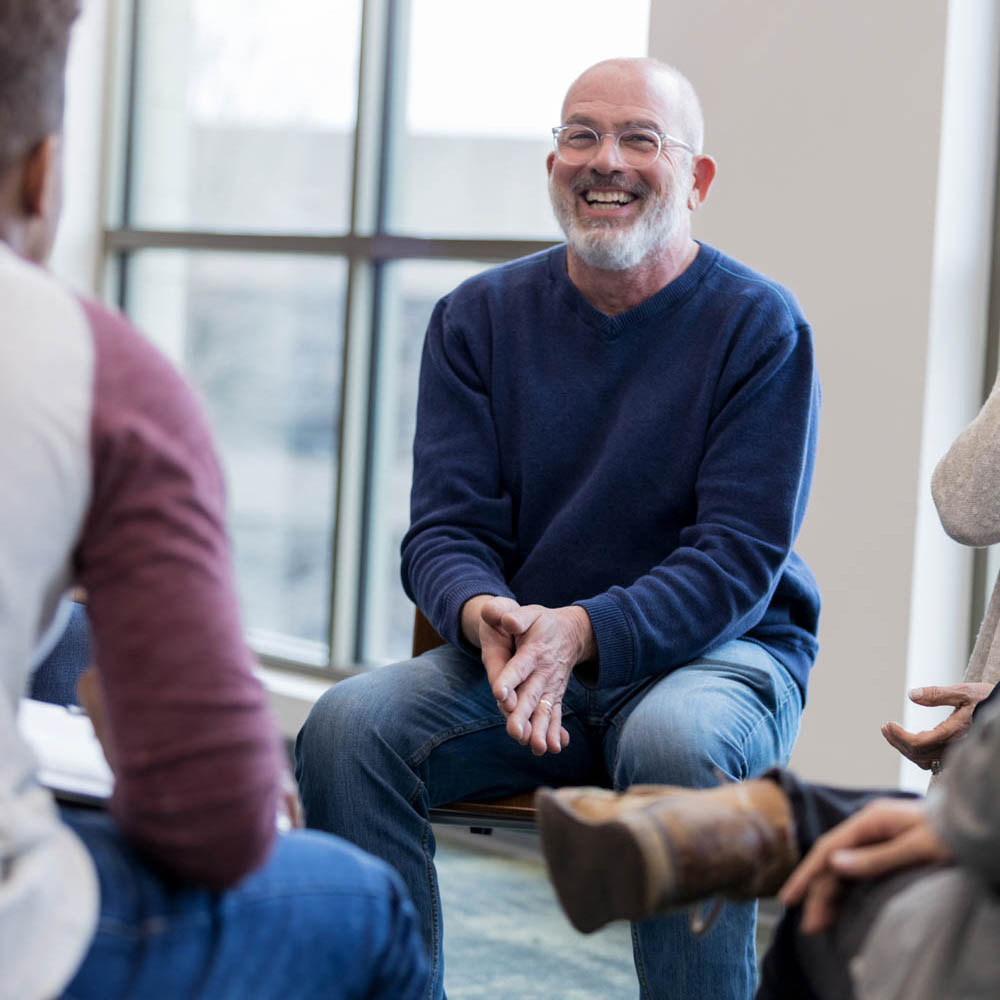 Laughing law enforcement officer seated in a group therapy session, illustrating the supportive community environment at Deer Hollow’s residential treatment centers and intensive outpatient programs.