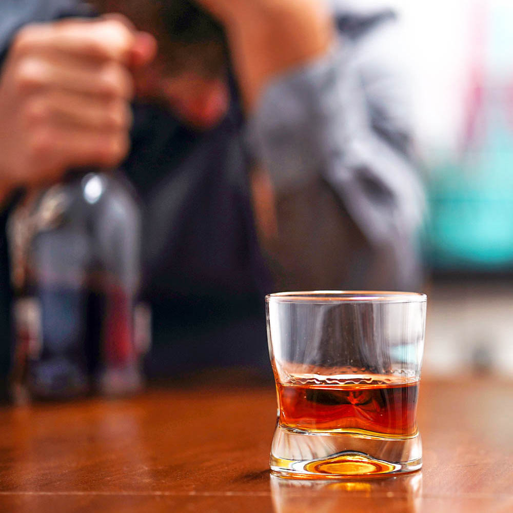 Off-duty law enforcement officer sitting in a bar, visibly intoxicated, drinking alcohol from a bottle and glass, highlighting alcohol addiction caused by unresolved trauma and the need for Deer Hollow’s specialized rehabilitation programs for first responders.