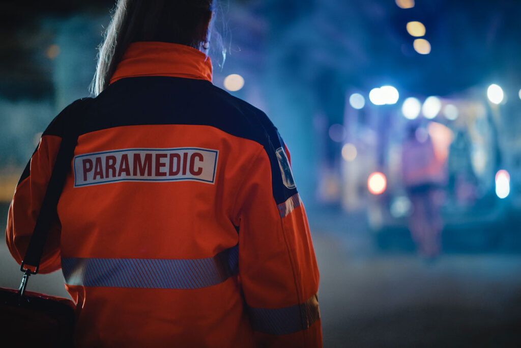 Female EMS paramedic standing at the scene of a fatal automobile accident, reflecting on the emotional toll of emergency medical service work.