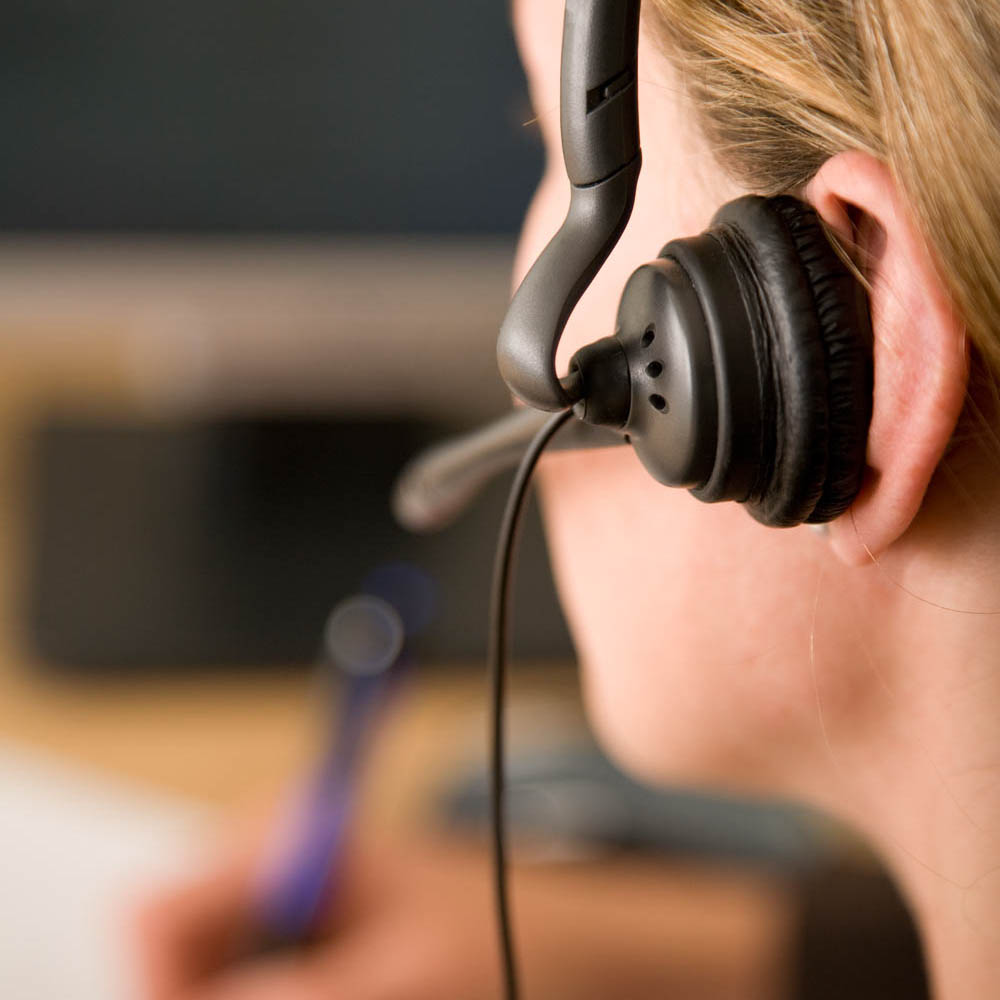 Close-up of a 911 dispatcher wearing a telephone headset, providing critical emergency services, highlighting the need for mental health support for dispatchers at Deer Hollow.