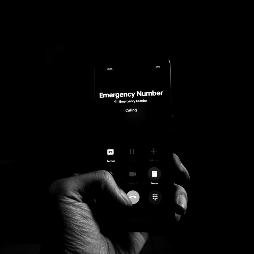 Hand dialing 911 emergency number on a mobile phone during a life-threatening situation, emphasizing the critical role of dispatchers and the mental health support available at Deer Hollow.