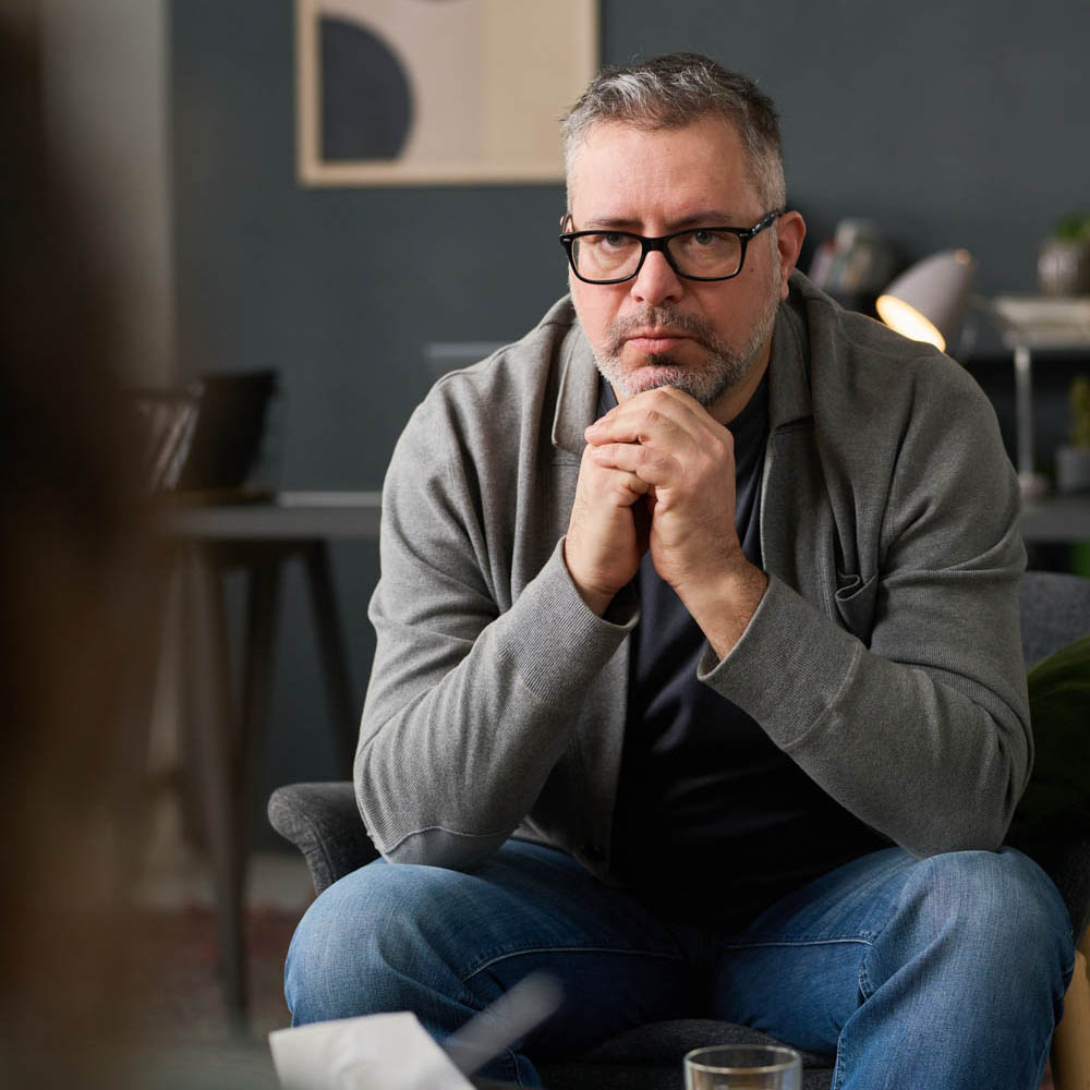 Male veteran sitting with hands folded under his chin, intently listening to a therapist, highlighting the personalized care offered at Deer Hollow’s residential treatment centers and intensive outpatient programs.