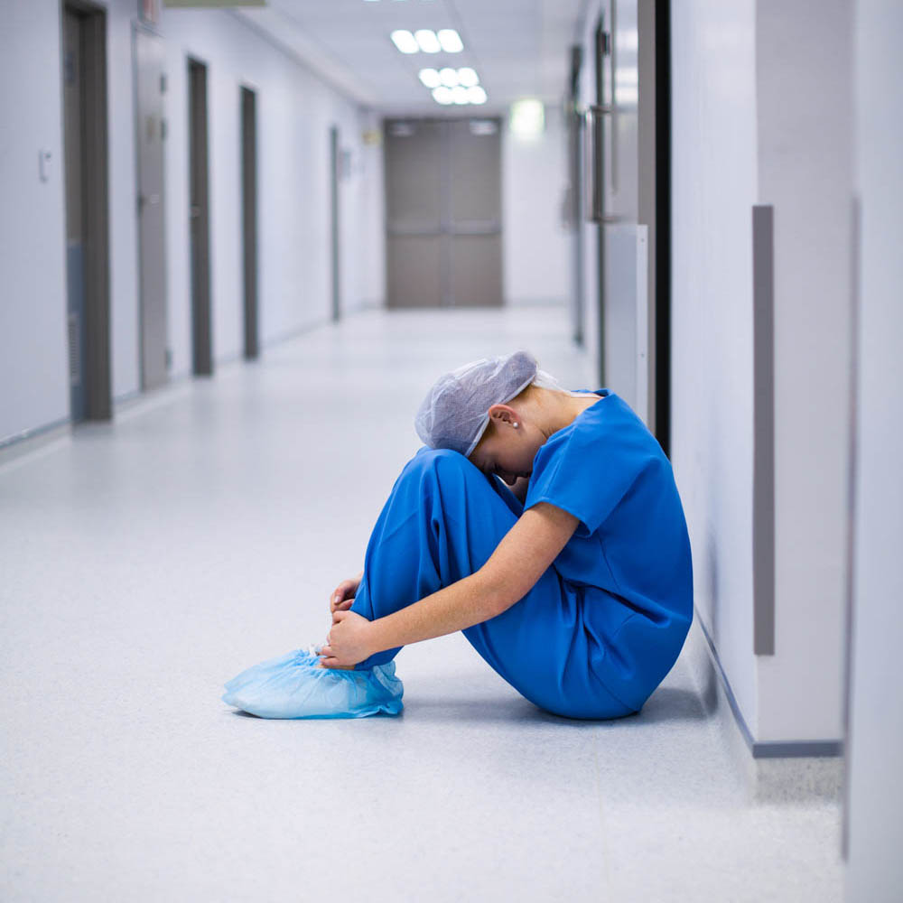 Operating room nurse sitting in a hospital hallway, experiencing trauma after the death of a patient, highlighting the need for Deer Hollow’s addiction and mental health treatment programs tailored for nurses dealing with PTSD and unresolved trauma.