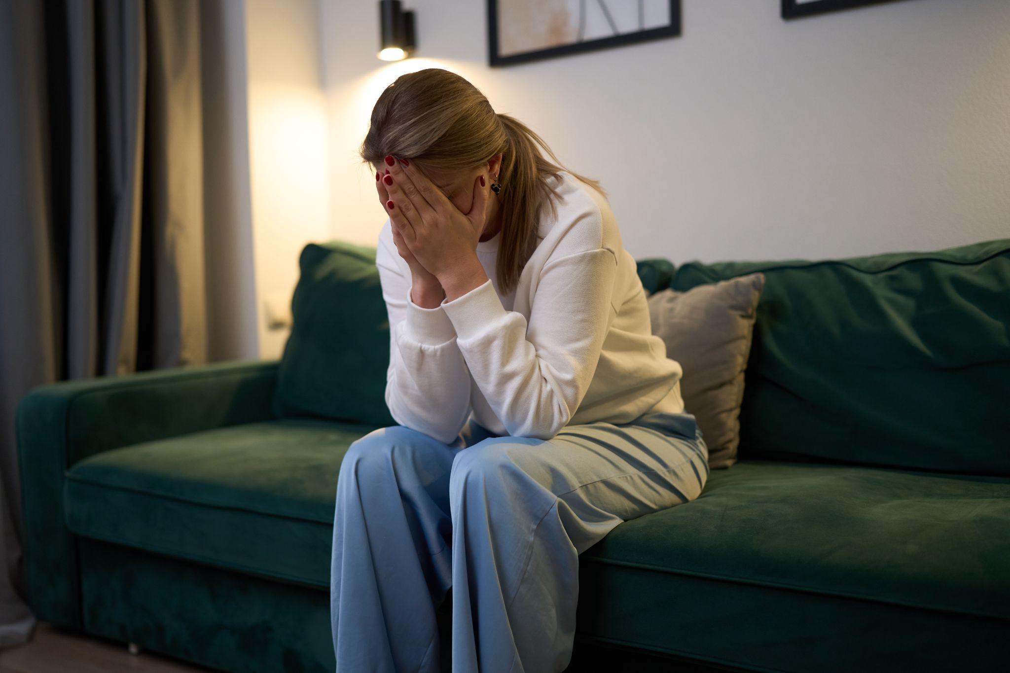 A distressed woman sitting on a green couch with her face buried in her hands.