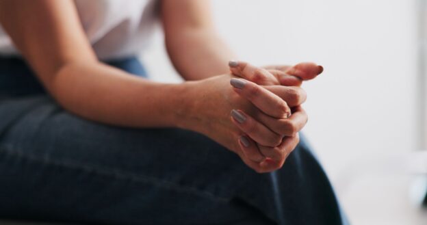 Close-up of a person sitting with their hands clasped together in their lap.