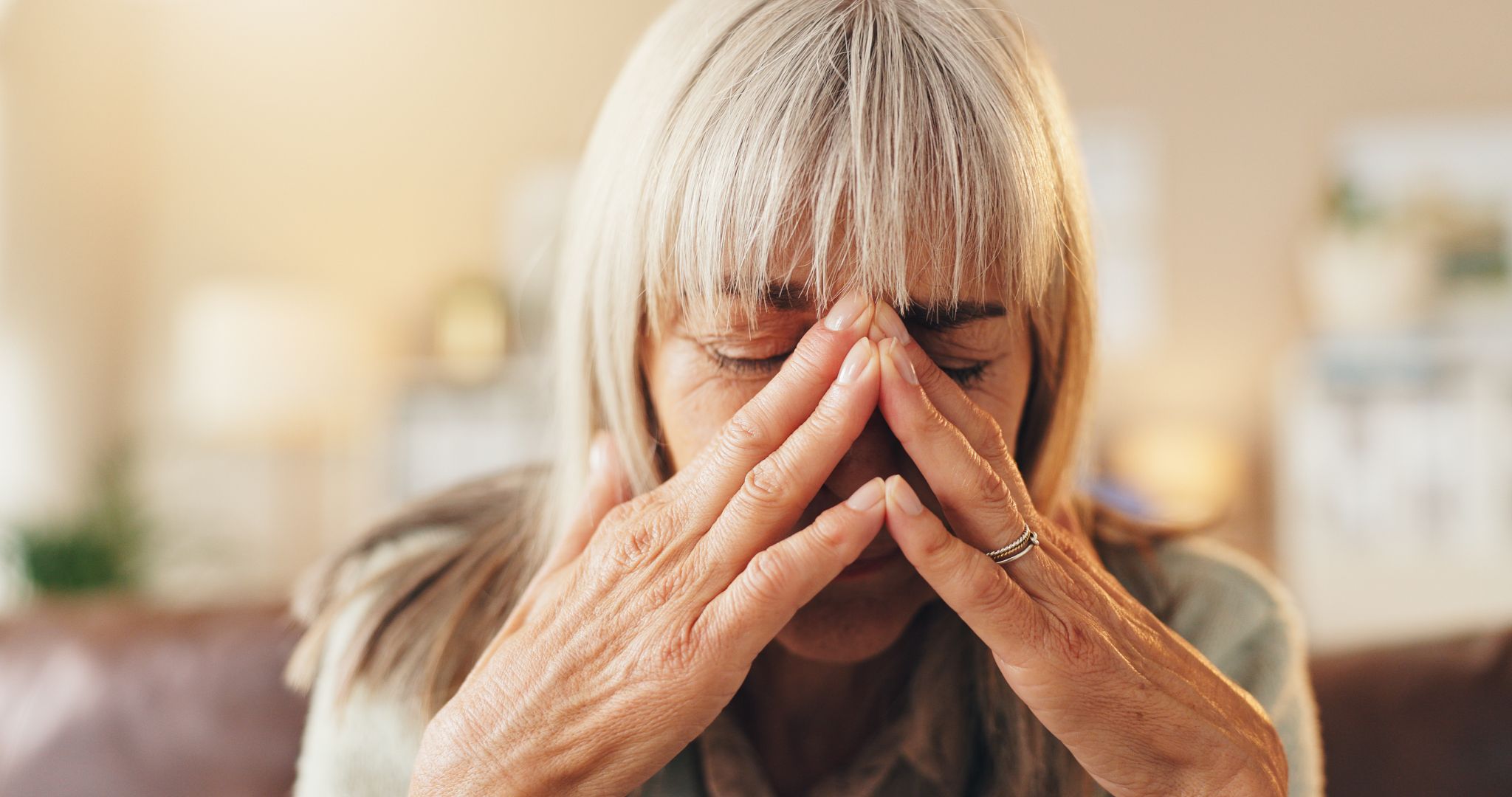 Close-up of a senior woman with blonde hair resting her face in her hands with her eyes closed in frustration or fatigue.